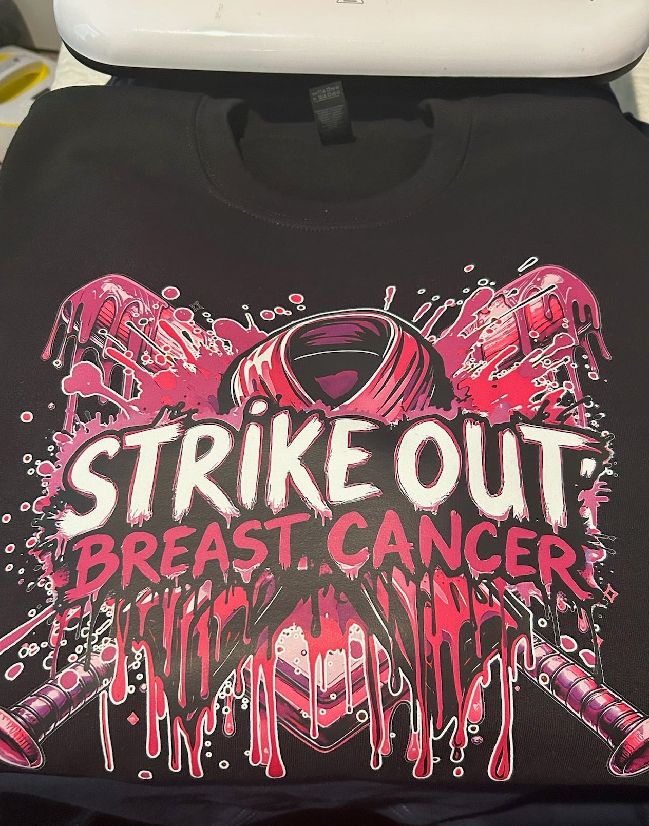 Black t-shirt with 'Strike Out Breast Cancer' design on a table.