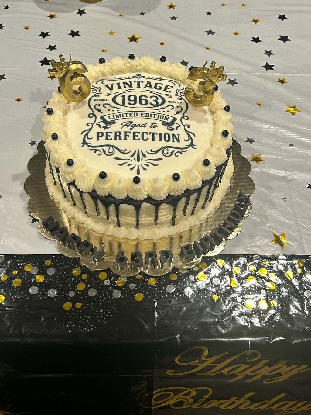 Two-tiered birthday cake with 'Vintage 1963' design on a decorative tablecloth.